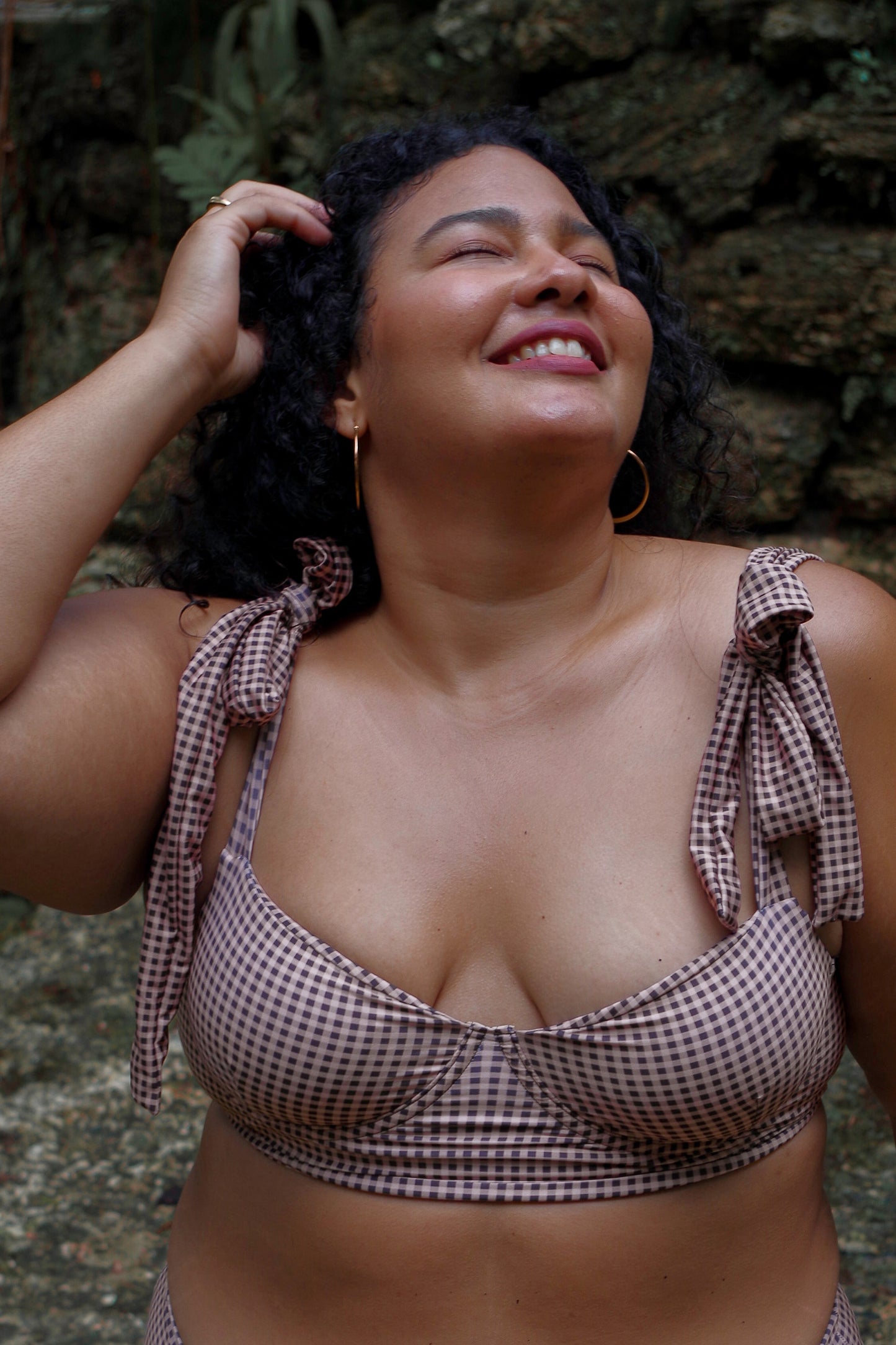 Woman wearing a checkered bikini top outdoors against a stone wall.