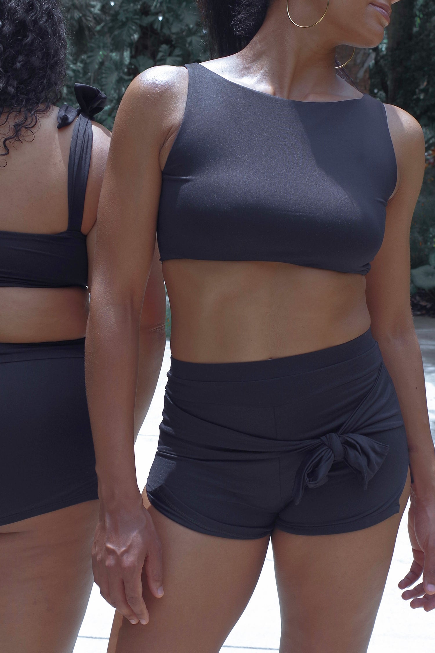 woman wearing cropped black tankini with removable padding and high waisted swim shorts